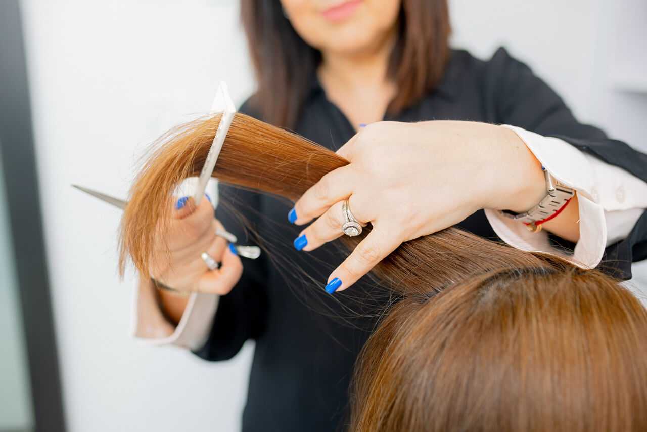 Hairdresser trimming a client's brown hair with scissors in a salon.