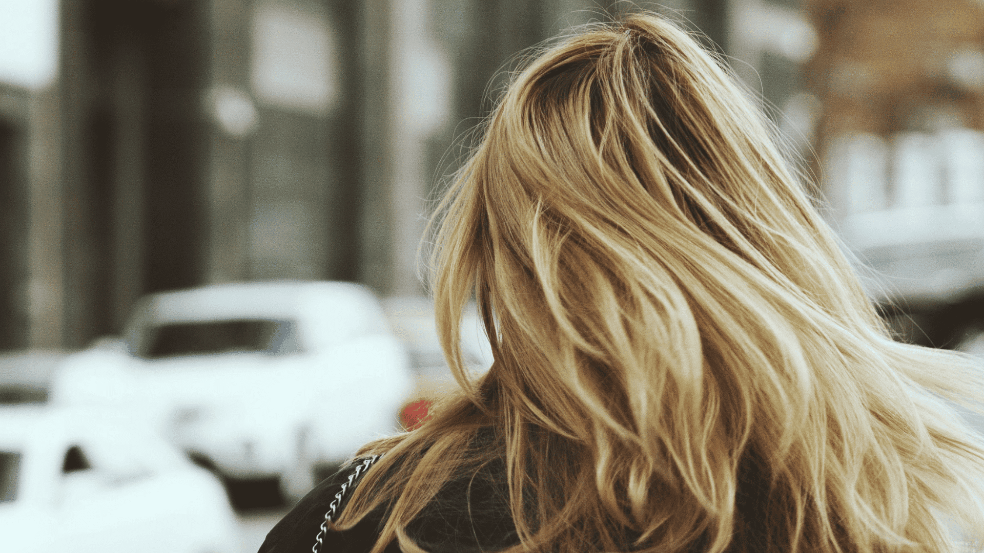 Back view of a person with long blonde hair walking in an urban street.